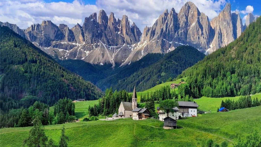 Paysage pittoresque des Dolomites avec l'église de Santa Maddalena, montagnes escarpées et vallées verdoyantes.