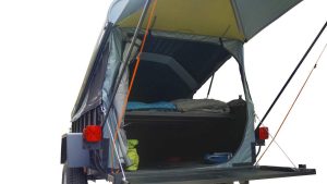 Vue intérieure du CrashPad installé sur une remorque : lit double surélevé avec matelas et sac de couchage, structure en toile tendue et toit rigide ouvert