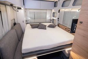 Lit double avec coussins dans l’intérieur moderne et lumineux de la caravane électrique Knaus YASEO, mettant en avant le confort et l’optimisation de l’espace.