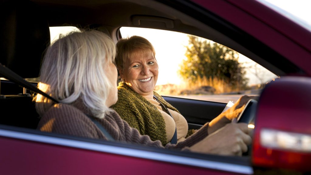 Deux femmes âgées souriantes assises dans une voiture, symbolisant la conduite des seniors et la sécurité routière.