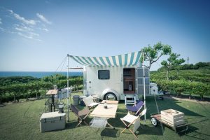Mini caravane japonaise X-Cabin 300 en aluminium aménagée pour le camping avec auvent et mobilier extérieur, vue sur mer