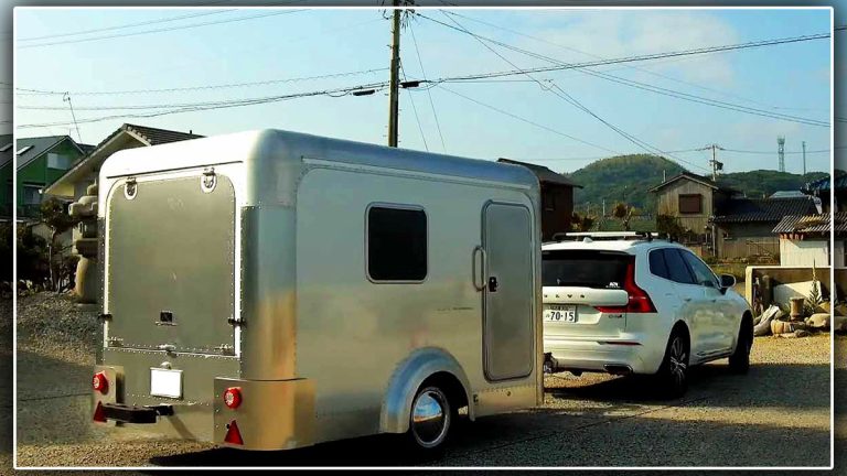 La mini caravane japonaise X-Cabin 300 en aluminium, tractée par une voiture blanche. Son design compact et léger en fait une alternative intéressante aux caravanes plus traditionnelles.