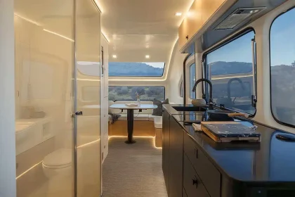 Vue latérale intérieure d'une caravane haut de gamme avec mobilier minimaliste, grande baie vitrée et espace cuisine tout équipé.
