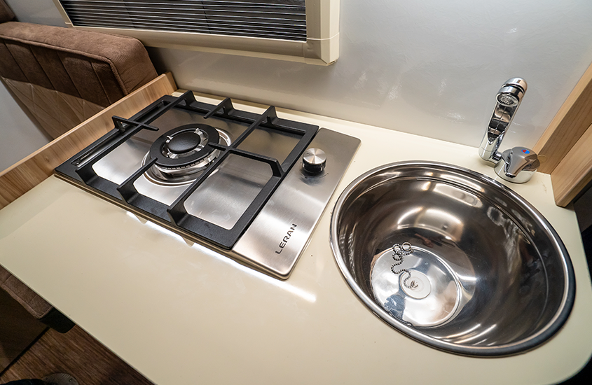 Espace cuisine du camping-car Lada Granta avec évier inox, plaque gaz et réfrigérateur intégré dans un aménagement minimaliste