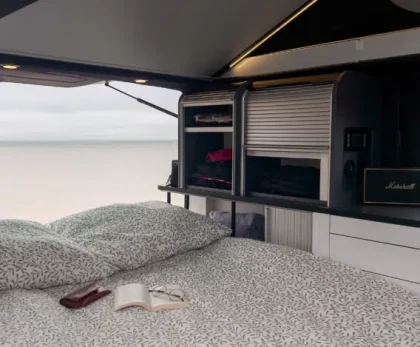 Lit double du van Hanroad TREK4 avec rangements intégrés, ouvert sur un paysage de plage.