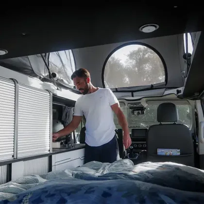 Un homme utilise la cuisine intérieure du van Hanroad TREK4, équipé d’un toit relevable et d’un lit confortable, parfait pour voyager à quatre.